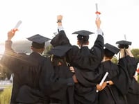 The back of graduates holding up their diplomas.
